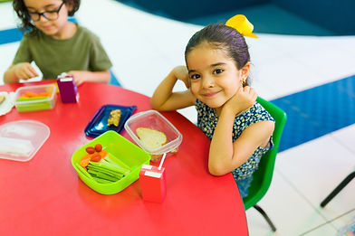 Adorable little girl smiling while eating her sandwich and healthy snacks during lunch bre