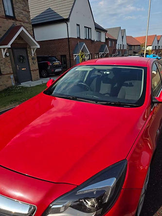 A red car with a new windshield outside a brick house