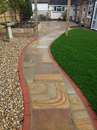 A garden path curves between a green lawn and pebble-covered side