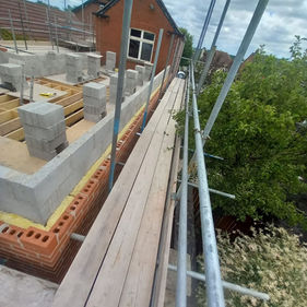 Scaffolded construction site beside a brick house under a cloudy sky