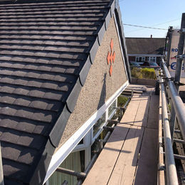 A gable roof with dark shingles and exposed pebble-dash cladding