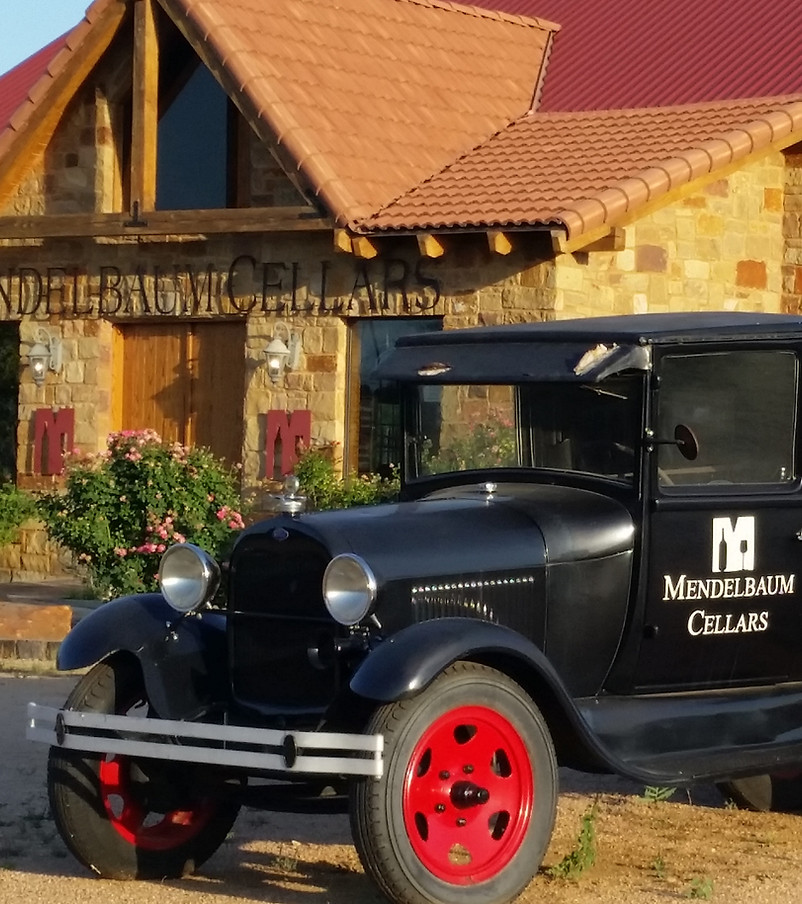 A vintage car is parked in front of a stone building with a red roof.