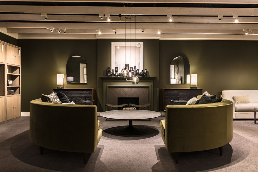 Green semi-circular couches sit opposite across from a large round black table.