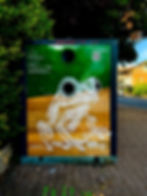 Grenouille peinte sur un conteneur de collecte vert et orange.