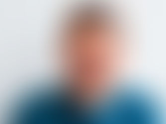 A man in a blue sweater holds his cheek, wincing in pain against a plain background, conveying discomfort.