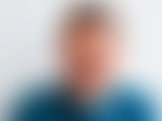 A man in a blue sweater holds his cheek, wincing in pain against a plain background, conveying discomfort.