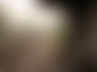 A man sits on a bench at an empty train station, looking at the tracks. It's overcast with muted colors, creating a lonely mood.