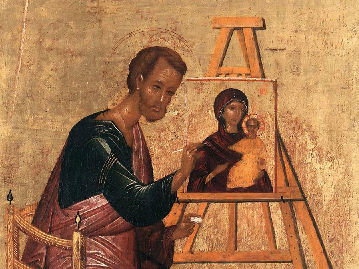 A person in robes paints a religious icon on a canvas; warm tones dominate the rustic setting, evoking a serene, devotional atmosphere.