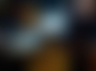 Woman sitting pensively in a dim blue room, sunlight streaming in. She wears a yellow sari. Clothes hang behind her, enhancing a reflective mood.