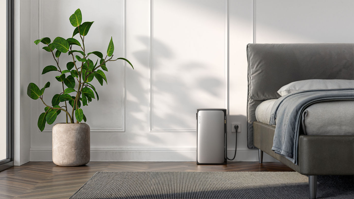 EcoFlow STREAM Batterie steht in einem Schlafzimmer neben einem Bett, eingesteckt in eine Steckdose.