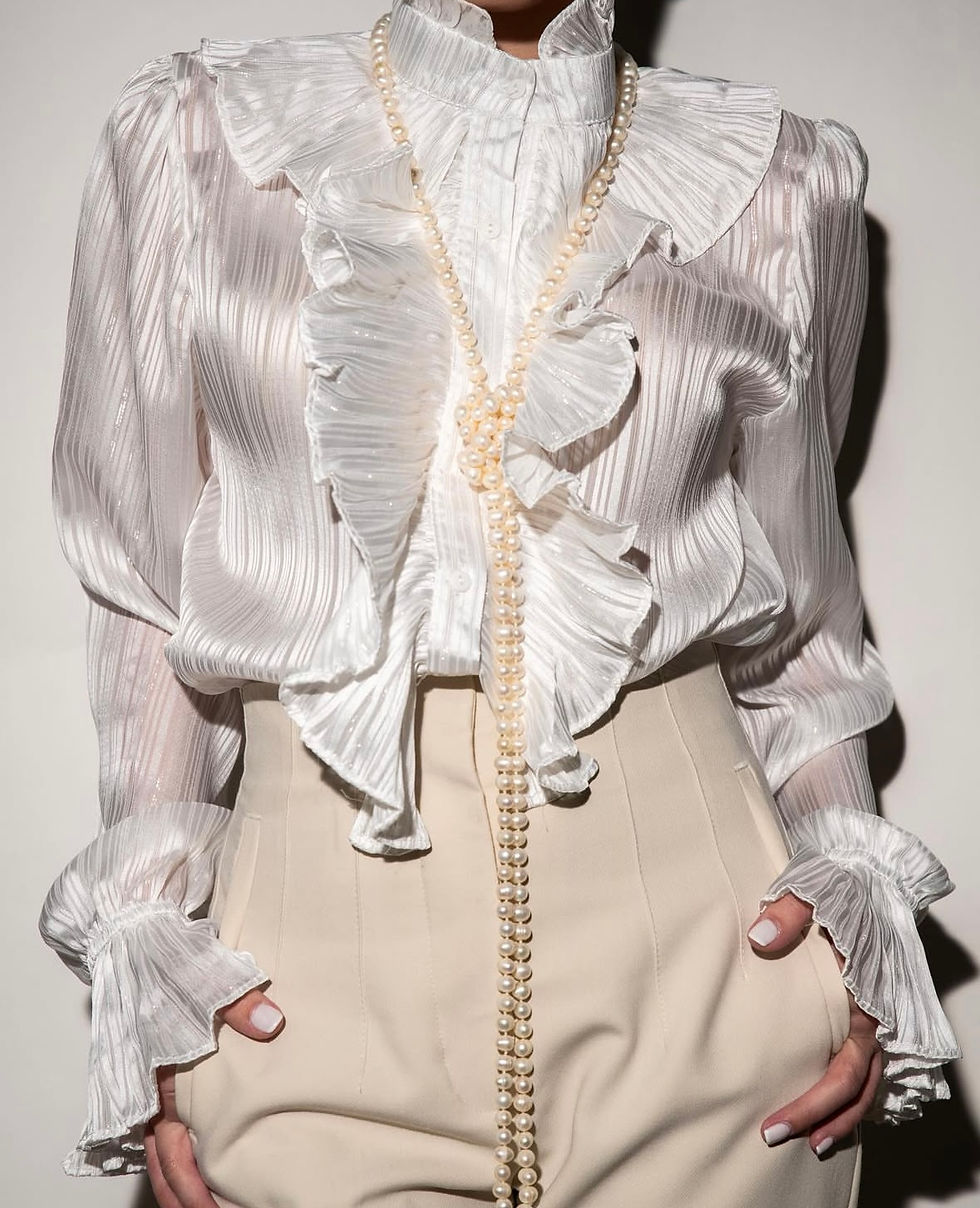 White sheer ruffled blouse with high collar and pearl necklace