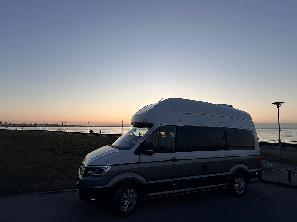 A camper van parked by the waterfront as the sun sets over the horizon, casting a peaceful glow across the sky and the sea.