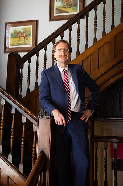 The Potash Law Firm's founder, Ben Potash, dressed in a suit and tie, standing on a staircase at his law office.