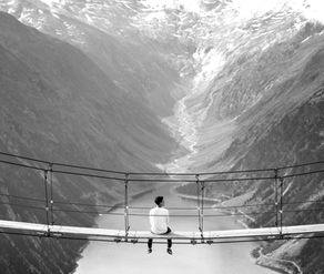man sitting on a walking bridge with a river far below
