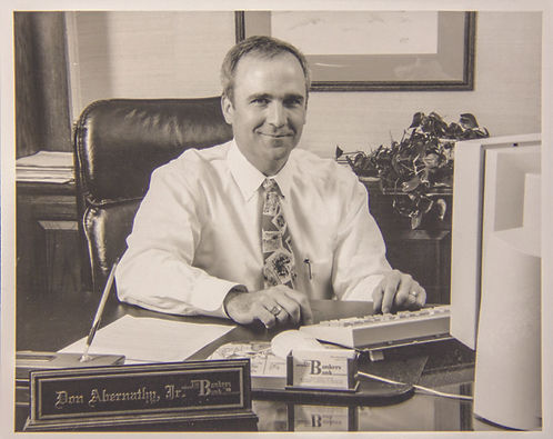 An old photo of a man sitting at a desk, smiling.