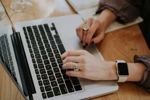 Close-up of a person typing on a MacBook laptop at a workspace
