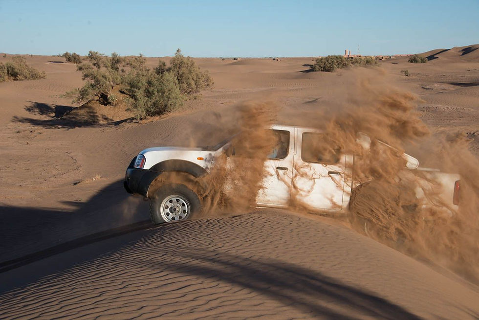 Pickup blanc embourbé dans les dunes du désert, soulevant un nuage de sable sous un ciel bleu.