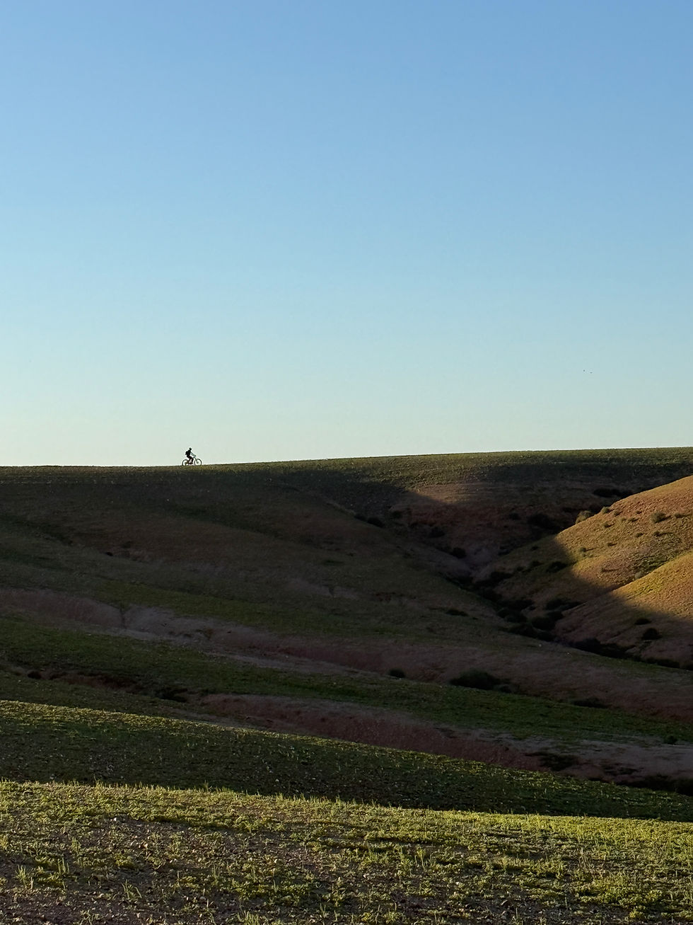 Cycliste solitaire sur une colline verdoyante sous un ciel bleu clair. Paysage vallonné et paisible, ambiance sereine.