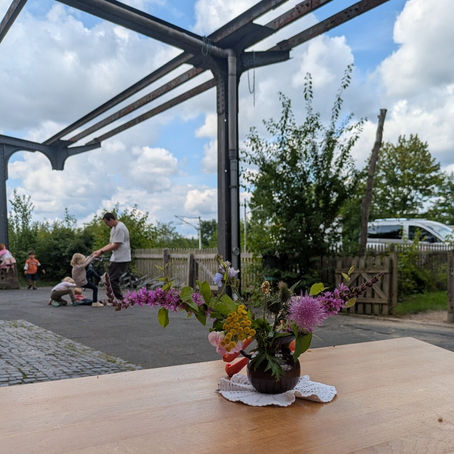 ein Schulhof, mit Blumen, die auf einem Tisch stehen. Im Hintergrund spielen Kinder