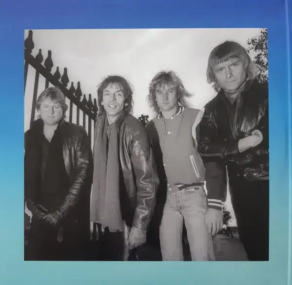 Thumbnail: Black and white photo of a four-member rock band posing by a gate.