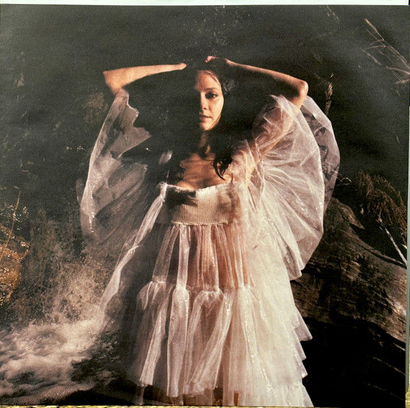 Thumbnail: Woman in white dress, arms raised, The One Collection, artistic, dramatic pose.