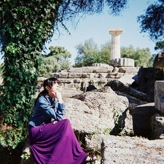 Christy sitting leaning with one hand under her chin having a thoughtful moment at a temple ruins in Greece
