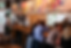 People sit at a wooden bar in a cozy café. Colorful mural above. A barista works behind the counter. Bright daylight through windows.