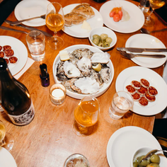 Dinner table with oysters, sliced sausage, olives, and drinks. People enjoy the meal, creating a cozy and convivial atmosphere.