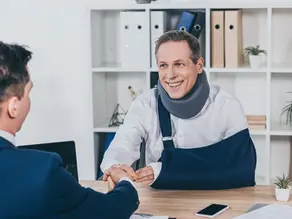 injured worker with a neck brace and arm sling smiling shaking hands with his workers comp lawyer