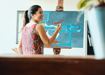 A Hispanic woman enjoying a painting class with a smile on her face.