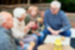Vier Senioren sitzen im glücklich im Garten und trinken gemeinsam einen Kaffee.