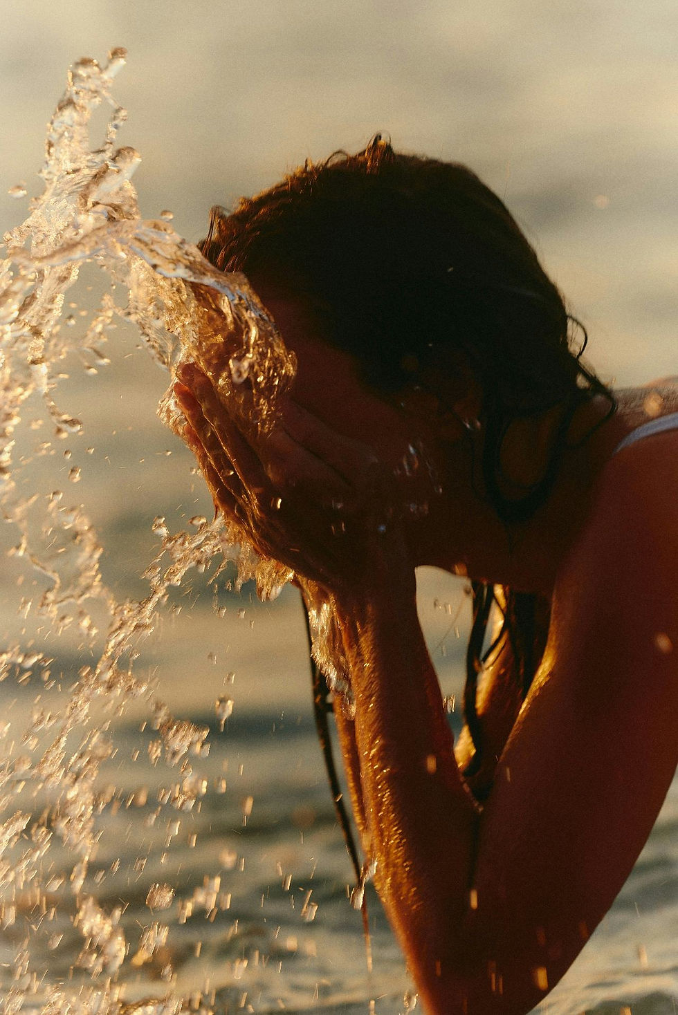 woman at sunset splashing water on her face with the ocean in the background