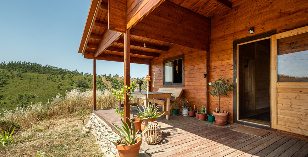 The covered porch creates a simple outdoor living space, connecting the wooden house with the surrou