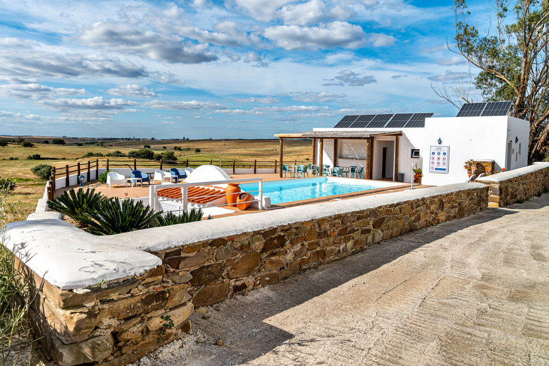 Swimming pool terrace with stone wall, sun loungers, and countryside views in Southern Portugal.