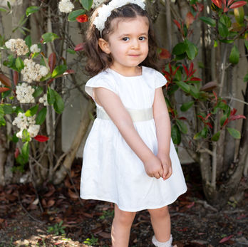 Young child standing outdoors in a white baptism dress before the ceremony.