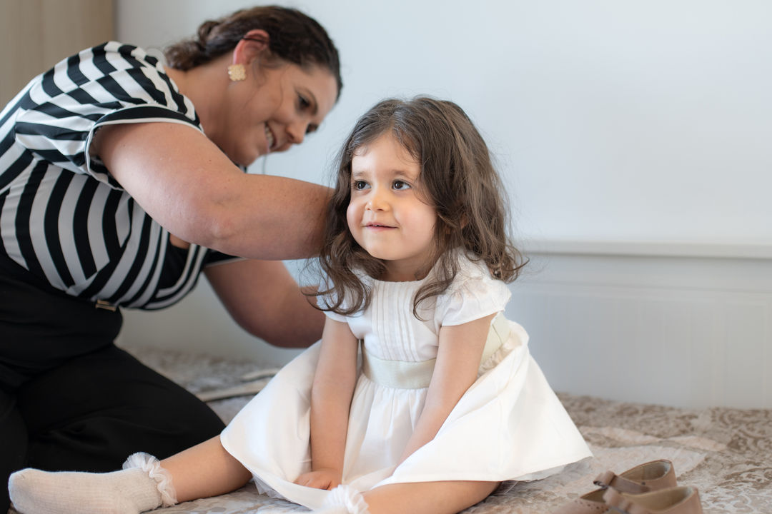 Child being dressed for baptism with a parent helping before the ceremony.