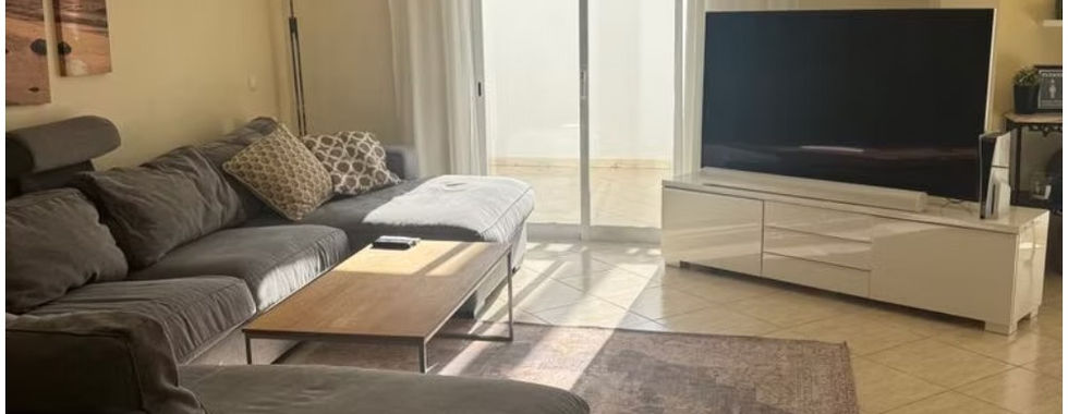 Smartphone photograph of a living room with a sofa, television and patio doors.