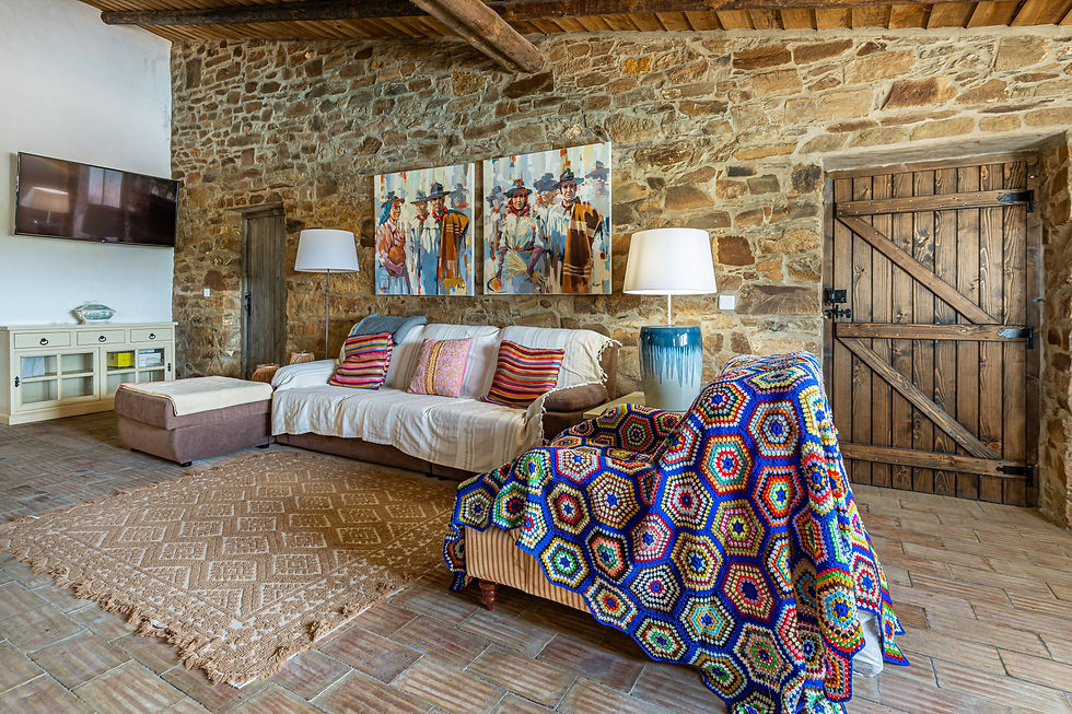 Sala de estar rústica com paredes de pedra, vigas de madeira no teto e assentos coloridos em Monte do Castelejo, no Alentejo.