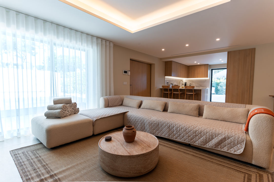 Modern Algarve villa living room with large sofa, warm lighting, and floor-to-ceiling curtains.