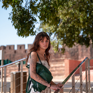 Young woman standing by railing with Silves Castle walls behind her during a travel photoshoot