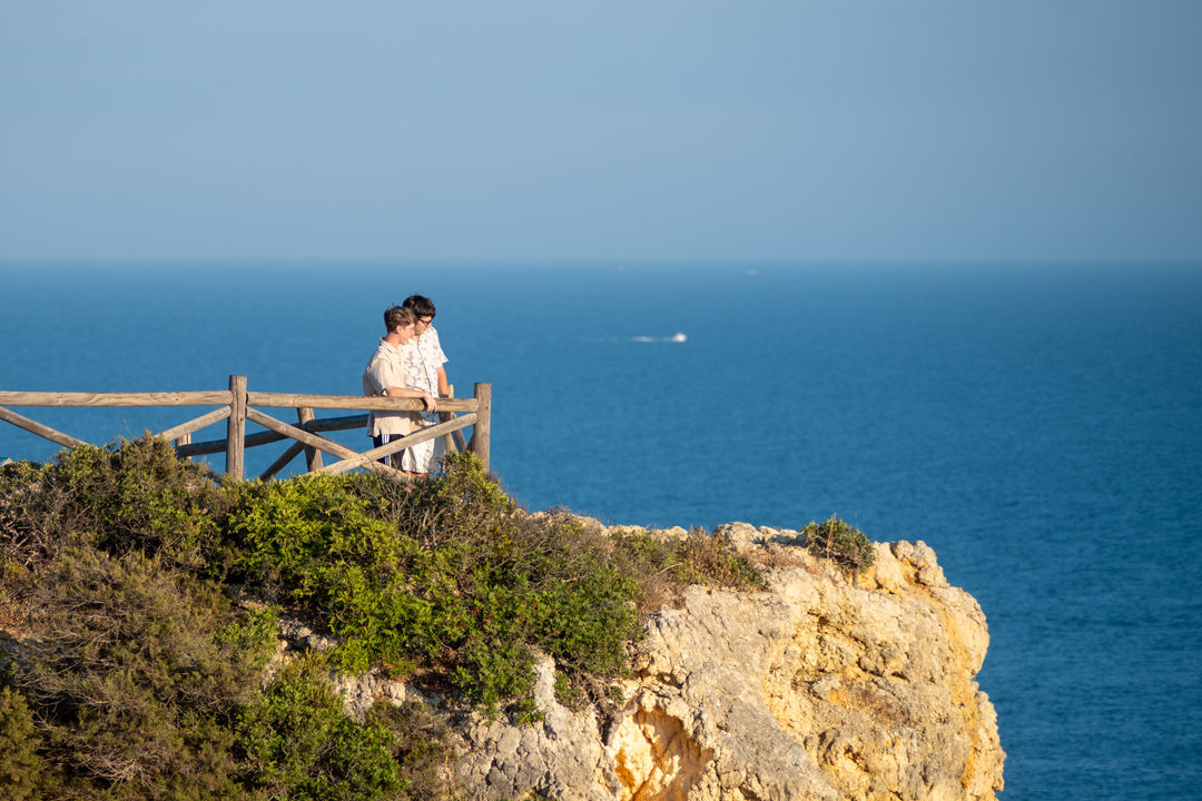Couple at a coastal viewpoint with wooden fence.