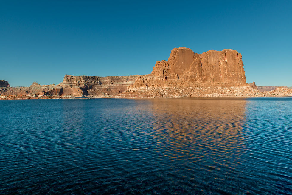A broad red sandstone butte rises beyond rippling deep blue water beneath a clear sky.
