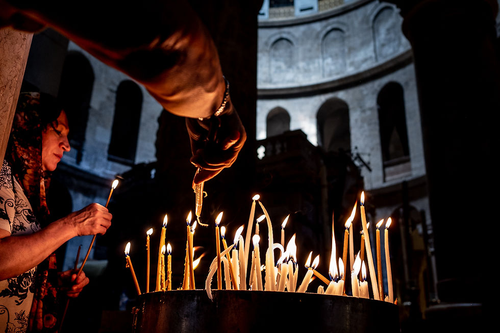 Hands reach toward a cluster of burning candles inside a dim stone church.
