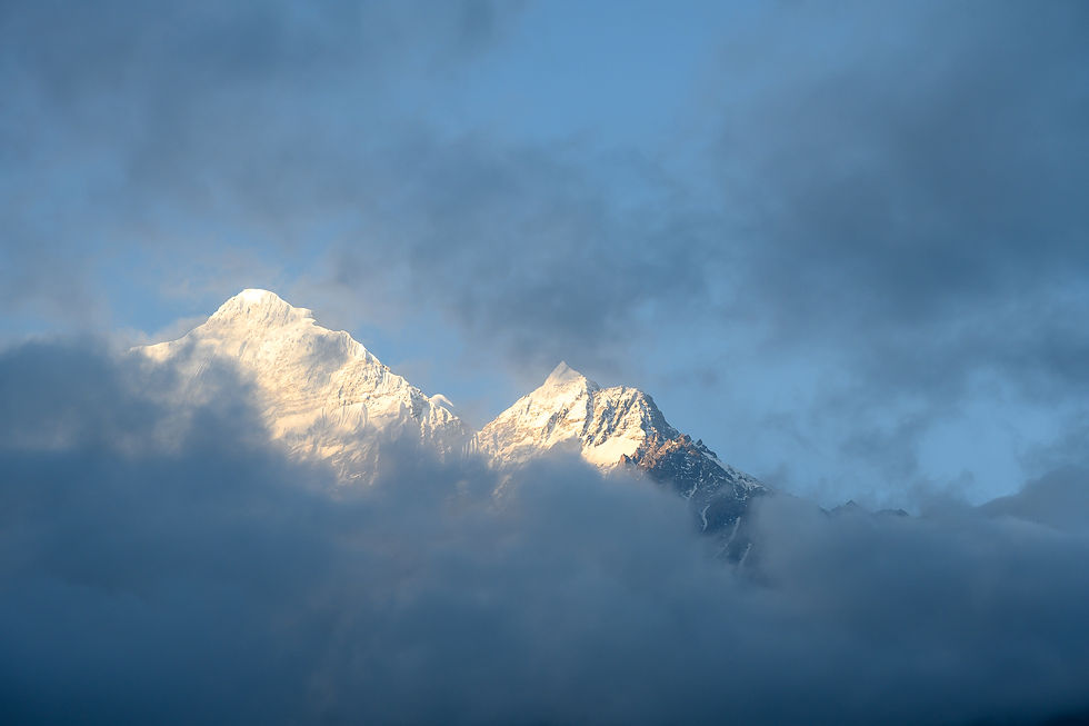 Snowy mountain summits catch warm light as they emerge from deep blue cloud and mist.