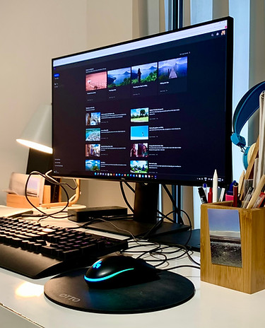 Computer sitting on a white desk with keyboard and mouse. Screen displays an editing program.
