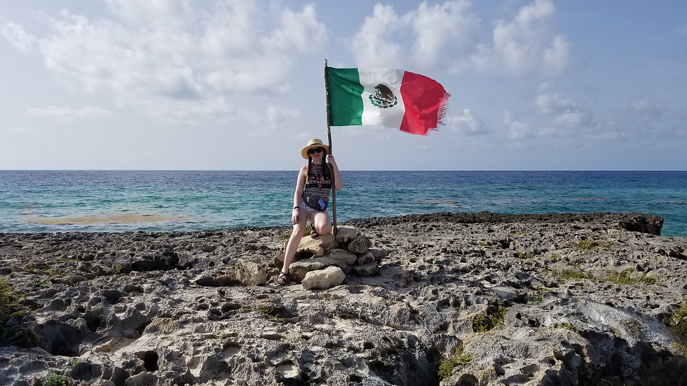 Girl standing near a flag on the rocky coast of Cozumel, Mexico