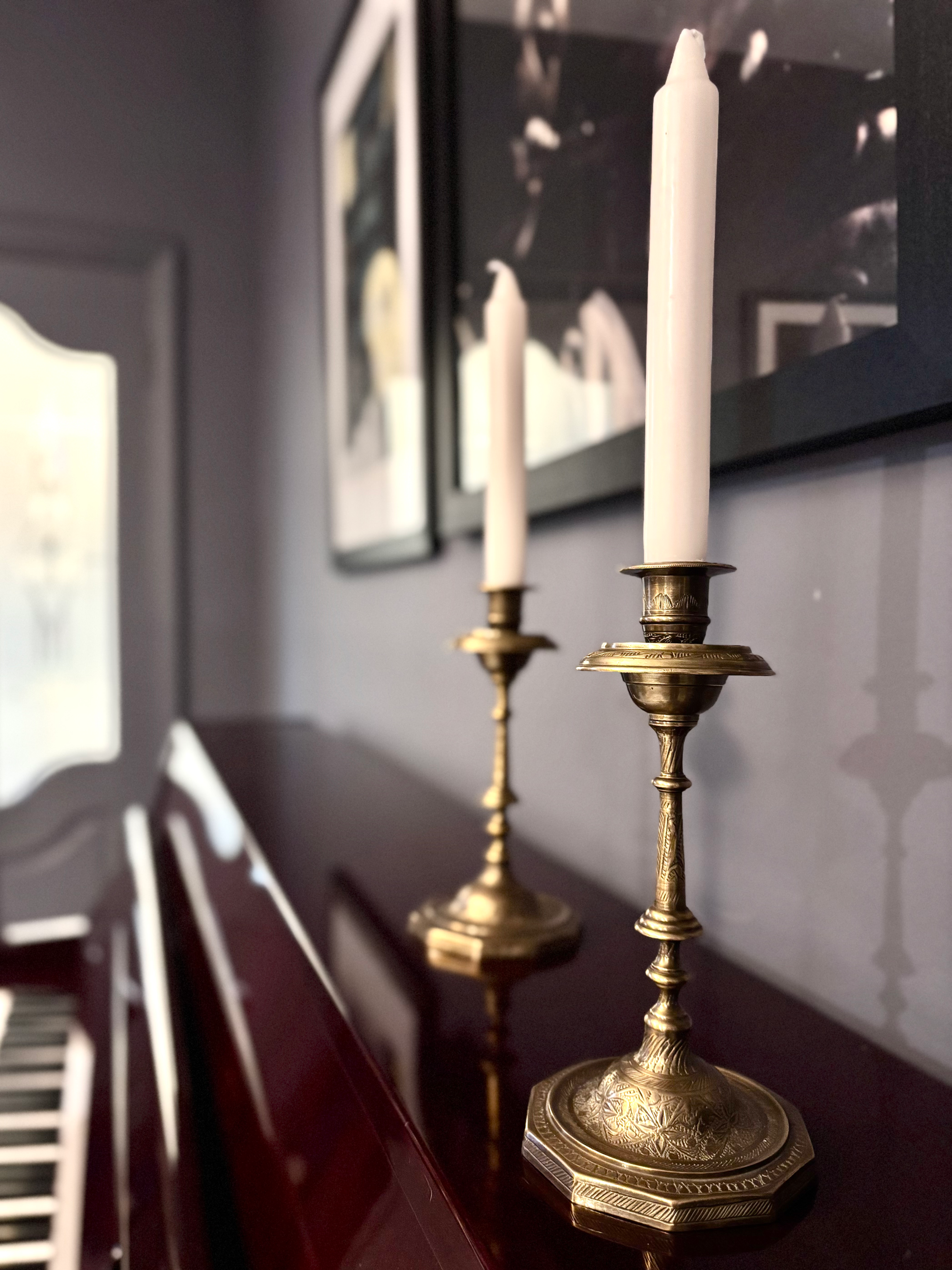 A pair of Anglo-Indian brass candlesticks placed on top of an upright piano