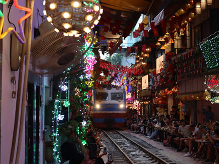 Colorful lanterns and people sitting along Hanoi Train Street as a blue and red train approaches