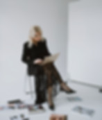 Blonde woman working on laptop, surrounded by magazines and books