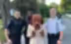 Three police officers pose with McGruff the Crime Dog, standing outdoors on a residential street.